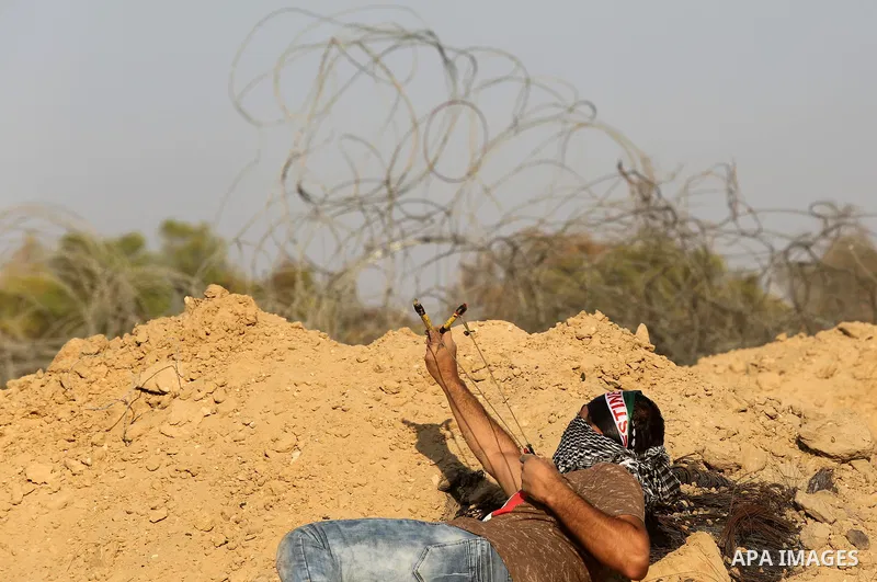 A Palestinian protester uses slingshots to hurl stones towards Israeli security forces during clashes near the border between Israel and Central Gaza Strip August 11, 2017. Photo by Ashraf Amra