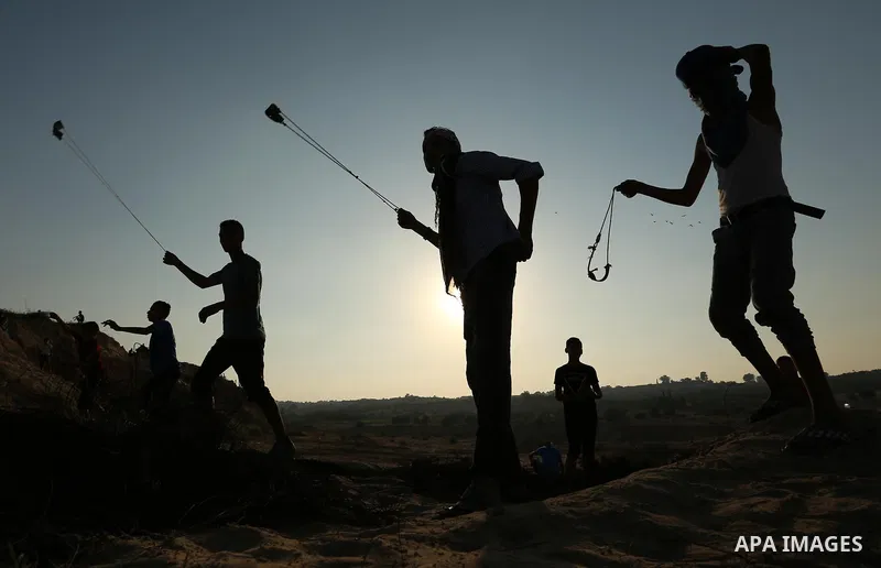 Palestinian protesters use slingshots to hurl stones towards Israeli security forces during clashes near the border between Israel and Central Gaza Strip August 11, 2017. Photo by Ashraf Amra