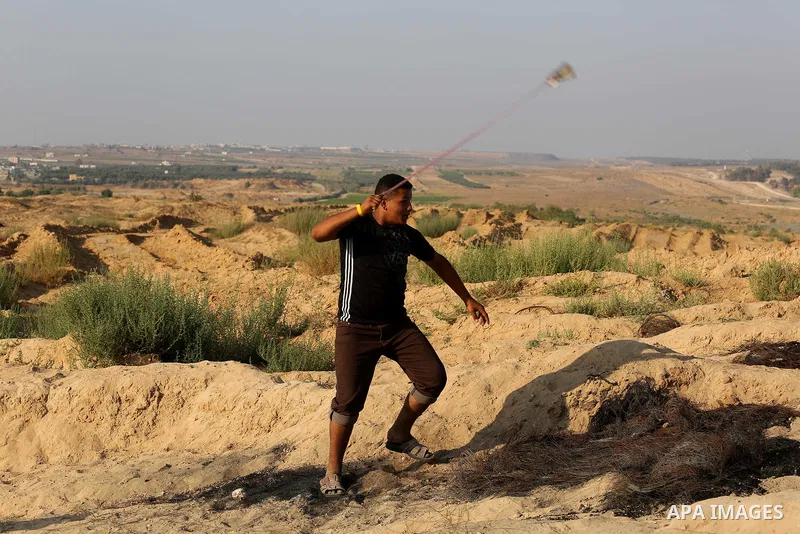 A Palestinian protester uses slingshots to hurl stones towards Israeli security forces during clashes near the border between Israel and Central Gaza Strip August 11, 2017. Photo by Ashraf Amra