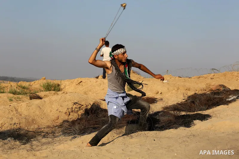 A Palestinian protester uses slingshots to hurl stones towards Israeli security forces during clashes near the border between Israel and Central Gaza Strip August 11, 2017. Photo by Ashraf Amra