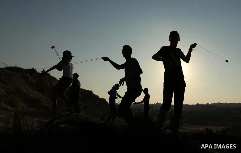 Palestinian protesters use slingshots to hurl stones towards Israeli security forces during clashes near the border between Israel and Central Gaza Strip August 11, 2017. Photo by Ashraf Amra