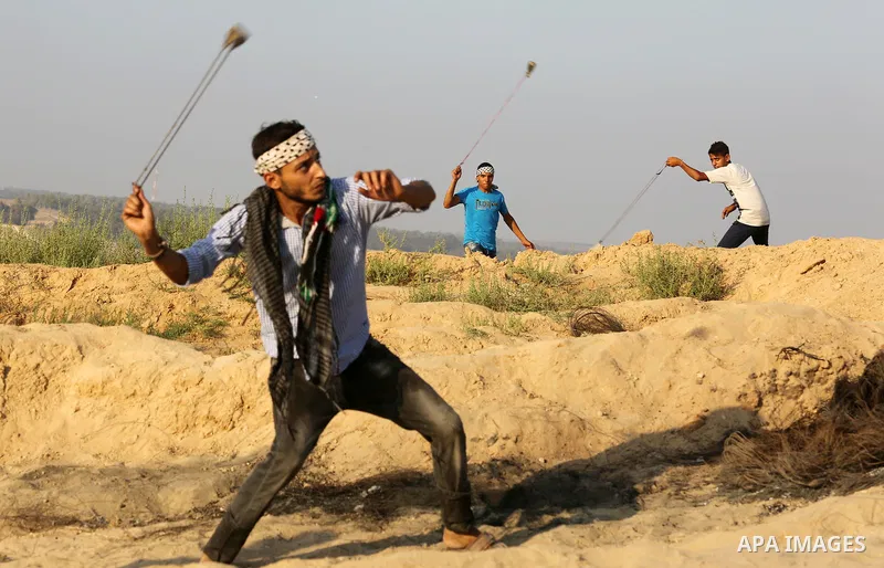 Palestinian protesters use slingshots to hurl stones towards Israeli security forces during clashes near the border between Israel and Central Gaza Strip August 11, 2017. Photo by Ashraf Amra