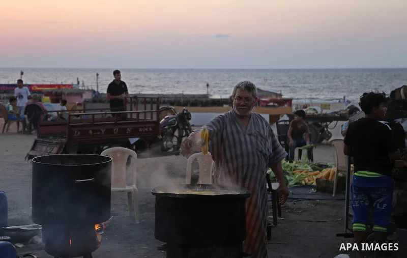 A Palestinian man sells boiled corn during the sunset at the beach of Gaza city on August 20, 2017. Photo by Ashraf Amra