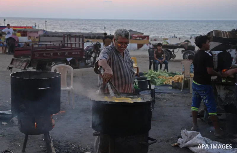 A Palestinian man sells boiled corn during the sunset at the beach of Gaza city on August 20, 2017. Photo by Ashraf Amra