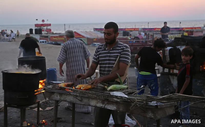A Palestinian man sells grilled corn during the sunset at the beach of Gaza city on August 20, 2017. Photo by Ashraf Amra