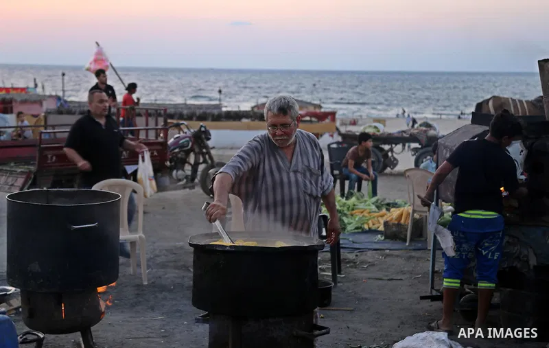 A Palestinian man sells boiled corn during the sunset at the beach of Gaza city on August 20, 2017. Photo by Ashraf Amra