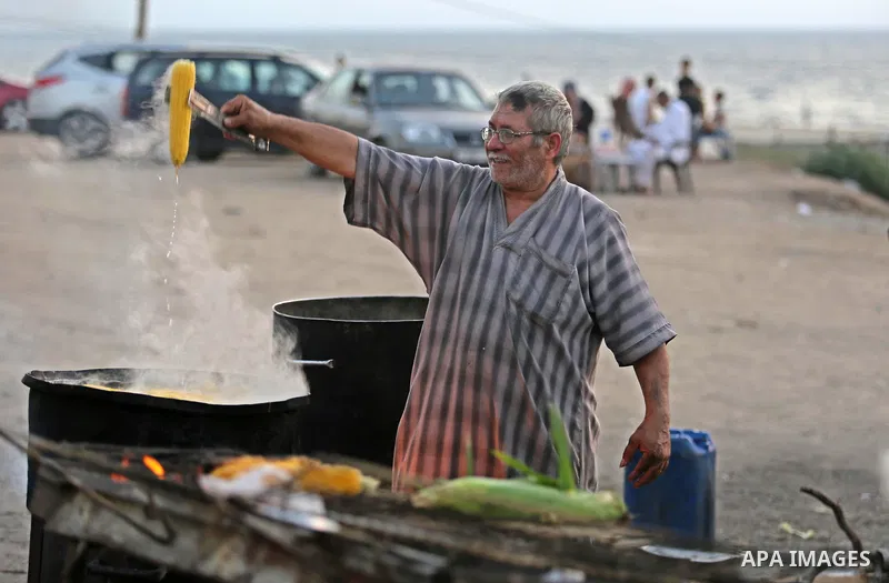 A Palestinian man sells boiled corn during the sunset at the beach of Gaza city on August 20, 2017. Photo by Ashraf Amra
