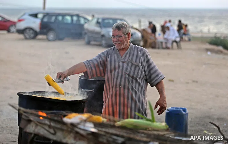 A Palestinian man sells boiled corn during the sunset at the beach of Gaza city on August 20, 2017. Photo by Ashraf Amra