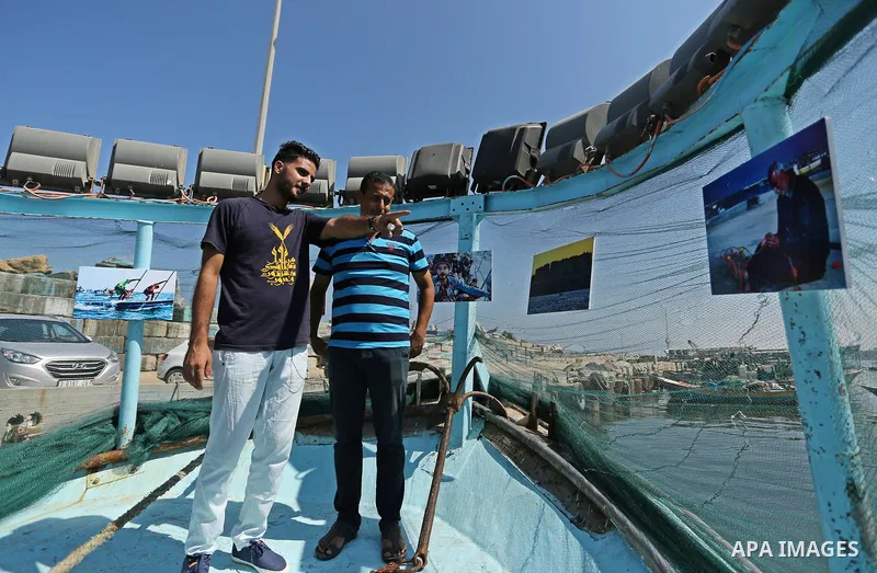 Palestinians attend a photo gallery on fishing boat, in Gaza seaport, on August 23, 2017. Photo by Ashraf Amra