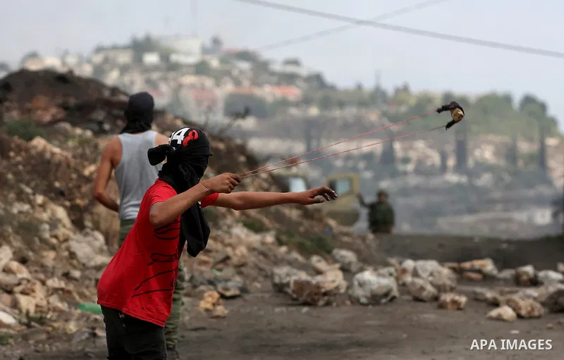 A Palestinian protester uses a slingshot to hurl stones towards Israeli security forces during clashes following demonstration against the expropriation of Palestinian land by Israel in the village of Kfar Qaddum, near N...