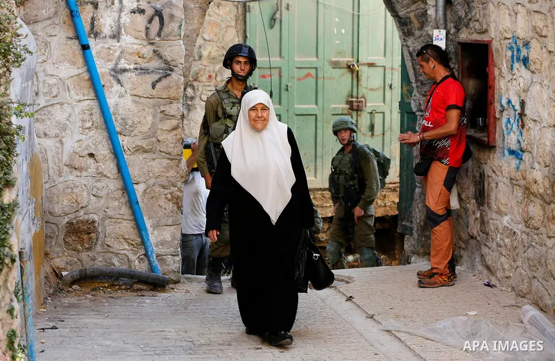 A Palestinian Woman walks as Israeli soldiers stand guard in the Old City of the West Bank city of Hebron on September 16, 2017. Photo by Wisam Hashlamoun