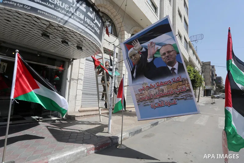 A Palestinian shop owner displays national flags and a poster bearing the portraits Palestinian Prime Minister Rami Hamdallah and Palestinian President Mahmoud Abbas on October 1, 2017, in Gaza city. Photo by Mohammed As...