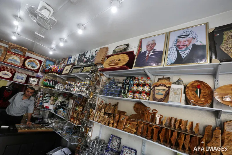 A Palestinian shop owner displays a poster bearing the portraits Palestinian Mahmoud Abbas and late Palestinian leader Yasser Arafat on October 1, 2017, in Gaza city. Photo by Mohammed Asad