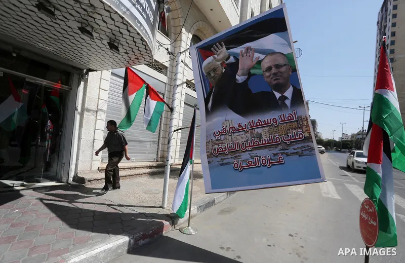 A Palestinian shop owner displays national flags and a poster bearing the portraits Palestinian Prime Minister Rami Hamdallah and Palestinian President Mahmoud Abbas on October 1, 2017, in Gaza city. Photo by Mohammed As...