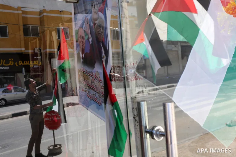 A Palestinian shop owner displays national flags and a poster bearing the portraits Palestinian Prime Minister Rami Hamdallah and Palestinian President Mahmoud Abbas on October 1, 2017, in Gaza city. Photo by Mohammed As...