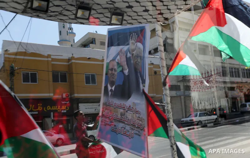A Palestinian shop owner displays national flags and a poster bearing the portraits Palestinian Prime Minister Rami Hamdallah and Palestinian President Mahmoud Abbas on October 1, 2017, in Gaza city. Photo by Mohammed As...