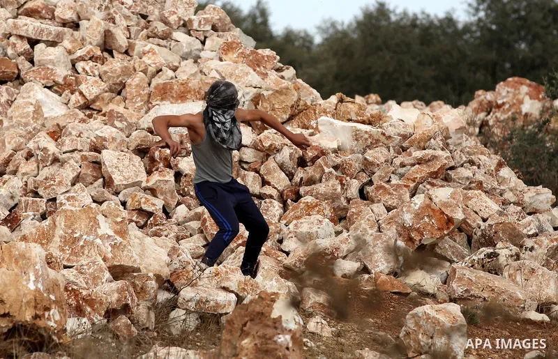A Palestinian protester uses a slingshot to hurl stones towards Israeli security forces during clashes following a demonstration against the expropriation of Palestinian land by Israel in the village of Kfar Qaddum, near...