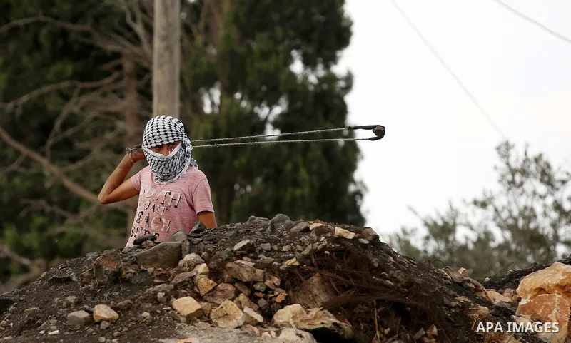 A Palestinian protester uses a slingshot to hurl stones towards Israeli security forces during clashes following a demonstration against the expropriation of Palestinian land by Israel in the village of Kfar Qaddum, near...
