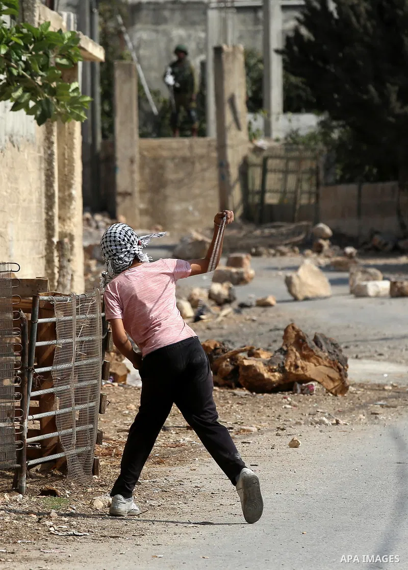A Palestinian protester uses a slingshot to hurl stones towards Israeli security forces during clashes following a demonstration against the expropriation of Palestinian land by Israel in the village of Kfar Qaddum, near...