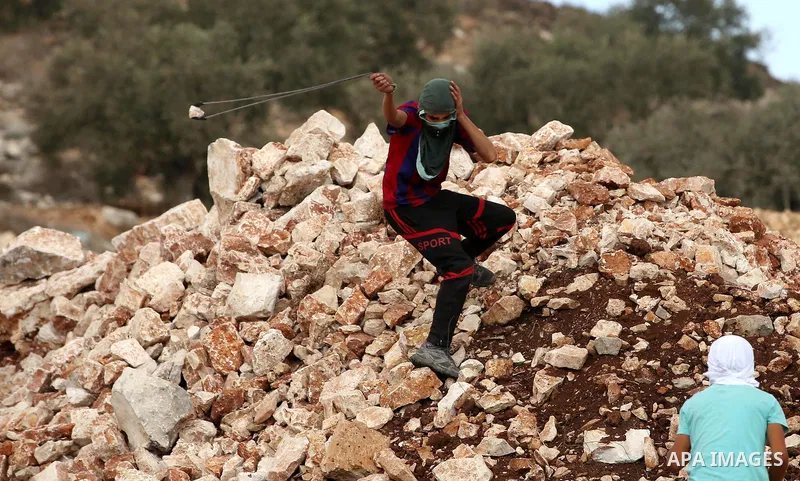 A Palestinian protester uses a slingshot to hurl stones towards Israeli security forces during clashes following a demonstration against the expropriation of Palestinian land by Israel in the village of Kfar Qaddum, near...