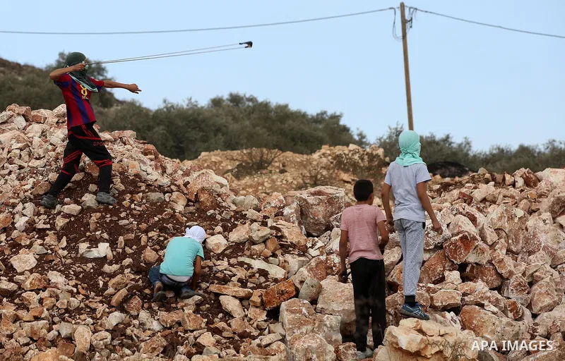A Palestinian protester uses a slingshot to hurl stones towards Israeli security forces during clashes following a demonstration against the expropriation of Palestinian land by Israel in the village of Kfar Qaddum, near...