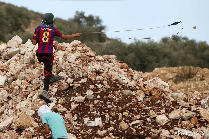 A Palestinian protester uses a slingshot to hurl stones towards Israeli security forces during clashes following a demonstration against the expropriation of Palestinian land by Israel in the village of Kfar Qaddum, near...