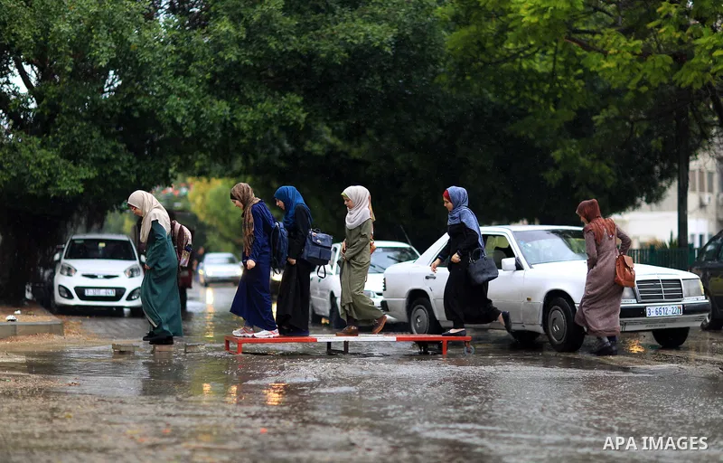 Palestinian students walk in a street flooded by rain water, in Gaza city on October 9, 2017. Photo by Atia Darwish