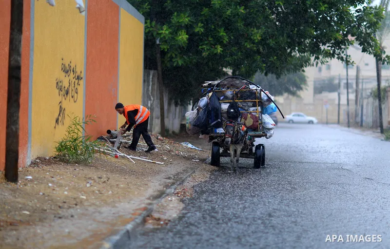 A Palestinian Cleaner works in a street during heavy rains, in Gaza city on October 9, 2017. Photo by Atia Darwish