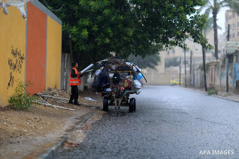 A Palestinian Cleaner works in a street during heavy rains, in Gaza city on October 9, 2017. Photo by Atia Darwish