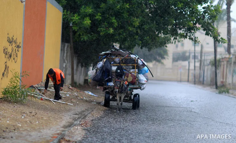 A Palestinian Cleaner works in a street during heavy rains, in Gaza city on October 9, 2017. Photo by Atia Darwish