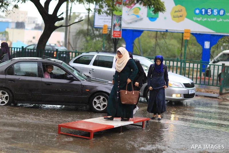 Palestinian students walk in a street flooded by rain water, in Gaza city on October 9, 2017. Photo by Atia Darwish