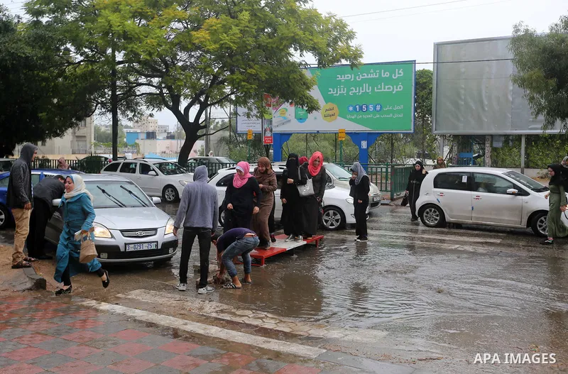 Palestinian students walk in a street flooded by rain water, in Gaza city on October 9, 2017. Photo by Atia Darwish