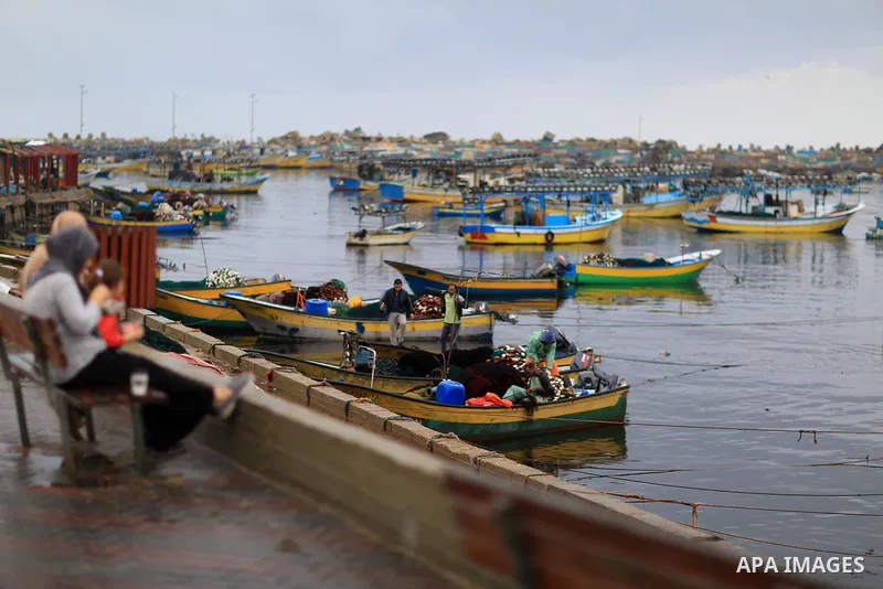Palestinians sit on the Gaza seaport during a rainy day, in Gaza city, on October 9, 2017. Photo by Atia Darwish