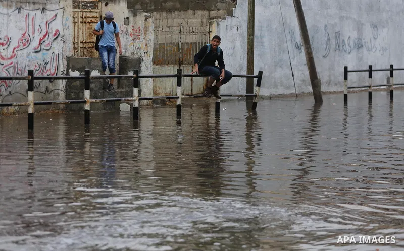 Palestinian students walk in a street flooded by rain water, in Gaza city on October 9, 2017. Photo by Mohammed Asad