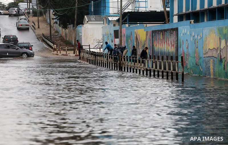 Palestinian students walk in a street flooded by rain water, in Gaza city on October 9, 2017. Photo by Mohammed Asad