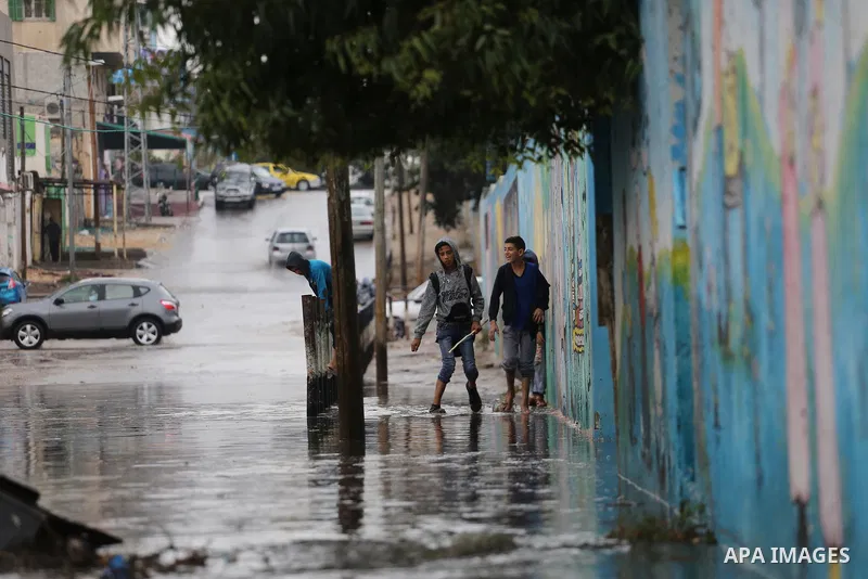 Palestinian students walk in a street flooded by rain water, in Gaza city on October 9, 2017. Photo by Mohammed Asad