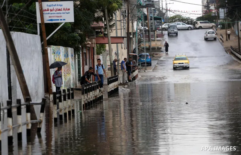 Palestinian students walk in a street flooded by rain water, in Gaza city on October 9, 2017. Photo by Mohammed Asad