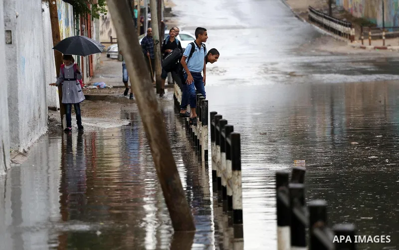 Palestinian students walk in a street flooded by rain water, in Gaza city on October 9, 2017. Photo by Mohammed Asad