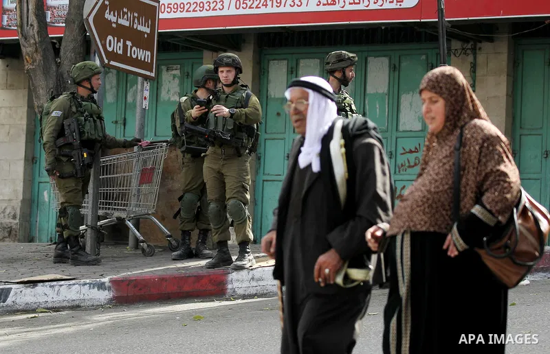Palestinians walk in front of Israeli soldiers as Israeli settlers walk towards the tomb of Atnaeil Ben Kinaz, a Jewish religious site during an annual pilgrimage organised by Israel's settler movement on the occasion of...
