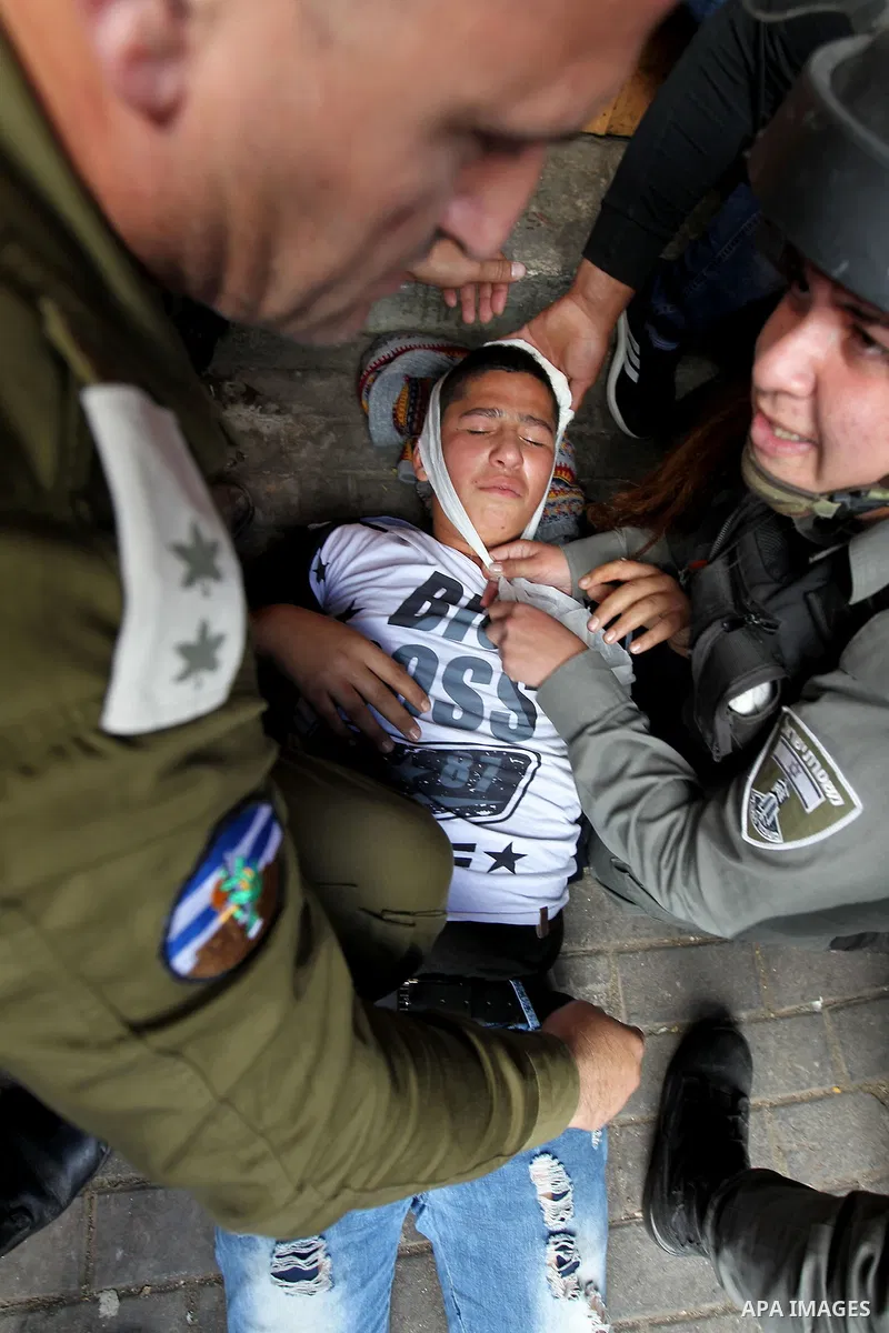 An injured Palestinian boy lies after an Israeli soldier hits him as Israeli settlers walk towards the tomb of Atnaeil Ben Kinaz, a Jewish religious site during an annual pilgrimage organised by Israel's settler movement...