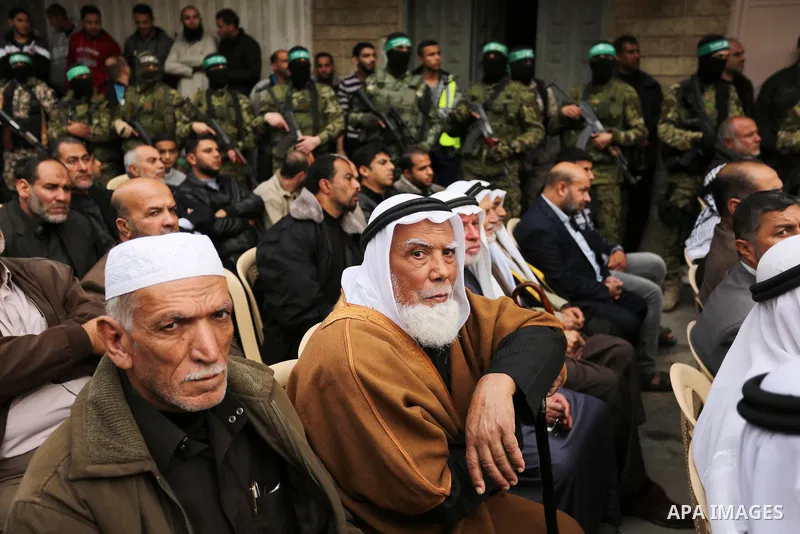 Palestinians watch as members of the Ezzedine al-Qassam Brigades, the military wing of the Palestinian Islamist movement Hamas take part during a military parade ahead of the 30th anniversary of Hamas' founding, in Khan...