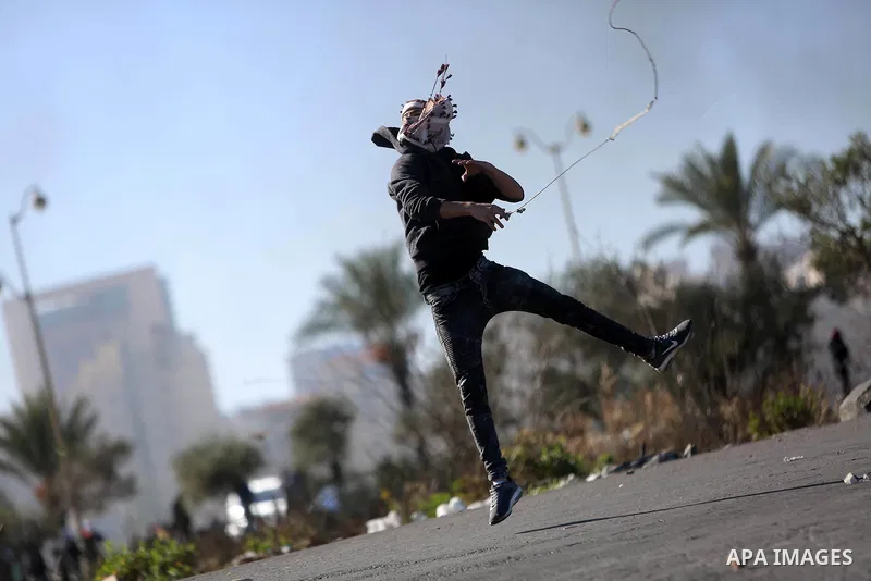 A Palestinian protester uses a slingshot to hurl stones towards Israeli security forces during clashes as Palestinians call for a "day of rage" in response to U.S. President Donald Trump's recognition of Jerusalem as Isr...