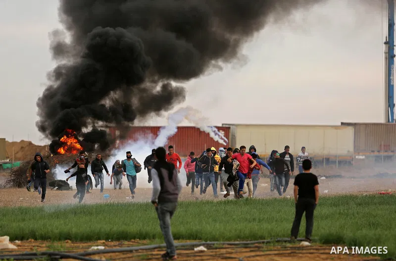 Palestinian protesters run through tear gas fumes during clashes with Israeli forces near the Israel-Gaza border east of the southern Gaza strip city of Khan Yunis on December 10, 2017, with Israeli heavy machinery seen...