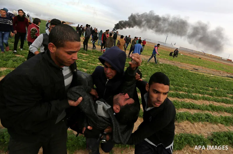 A wounded Palestinian protester is evacuated during clashes with Israeli forces near the Israel-Gaza border east of the southern Gaza strip city of Khan Yunis on December 10, 2017, with Israeli heavy machinery seen on th...