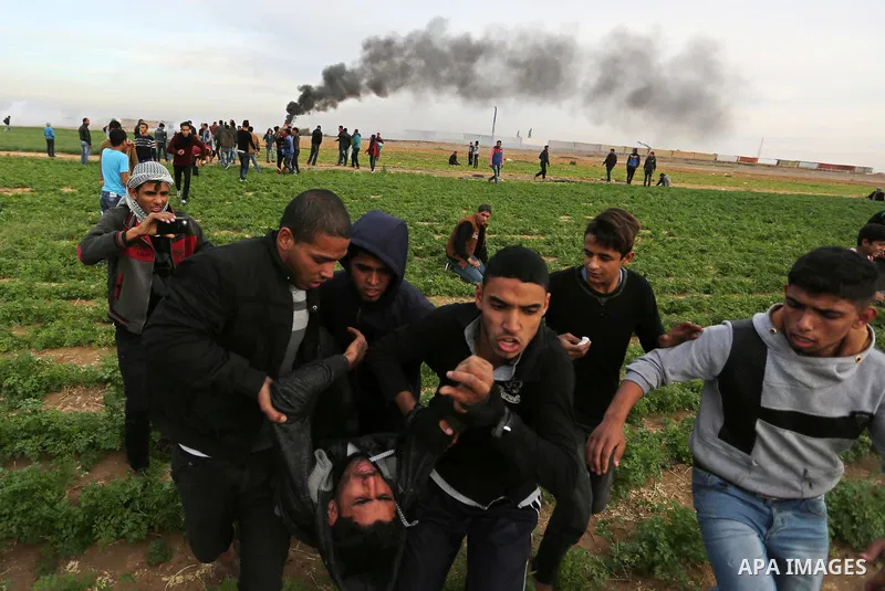 A wounded Palestinian protester is evacuated during clashes with Israeli forces near the Israel-Gaza border east of the southern Gaza strip city of Khan Yunis on December 10, 2017, with Israeli heavy machinery seen on th...