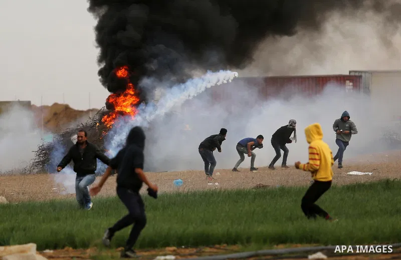 Palestinian protesters run through tear gas fumes during clashes with Israeli forces near the Israel-Gaza border east of the southern Gaza strip city of Khan Yunis on December 10, 2017, with Israeli heavy machinery seen...