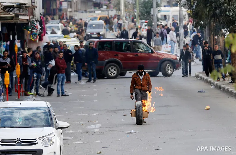 A masked Palestinian protester rolls a flaming tire during clashes with Israeli secrity forces behind a checkpoint in the city centre of the West Bank town of Hebron on December 11, 2017 as demonstrations continue to fla...
