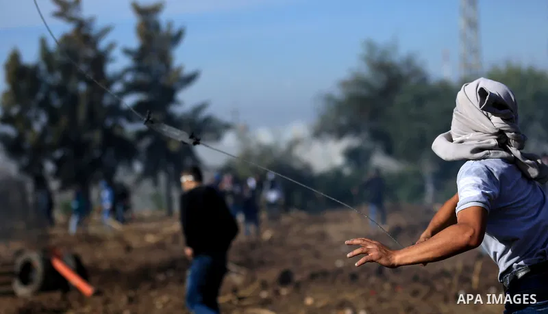 A Palestinian protester uses a slingshot to hurl stones towards Israeli security forces during clashes in the West Bank town of Tulkarem, following a demonstration against US President Donald Trump's decision to recognis...