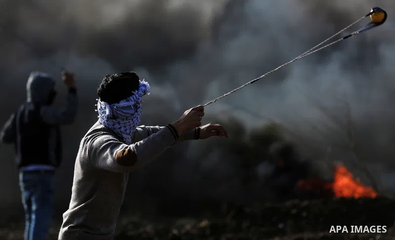 A Palestinian protester uses a slingshot to hurl stones towards Israeli security forces during clashes in the West Bank town of Tulkarem, following a demonstration against US President Donald Trump's decision to recognis...