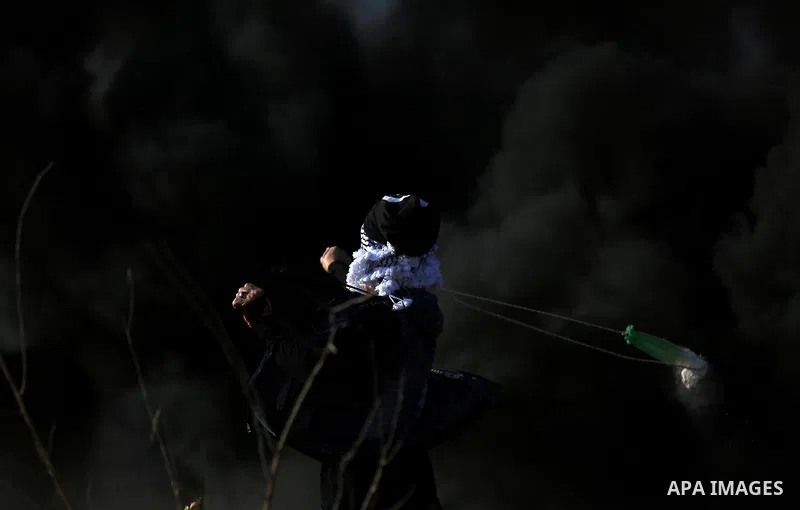 A Palestinian protester uses a slingshot to hurl stones towards Israeli security forces during clashes in the West Bank town of Tulkarem, following a demonstration against US President Donald Trump's decision to recognis...